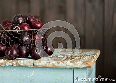 Ripe plums in a basket on a wooden background. Stock Photo