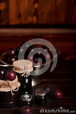 Ripe plums and jars with plum jam on a wooden background. Stock Photo