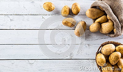 Ripe potatoes in burlap sack freely lying on board. Stock Photo