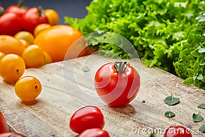 Ripe cherry tomato on a wooden cutting board surrounded by lettuce, basil leaves and yellow tomatoes Stock Photo