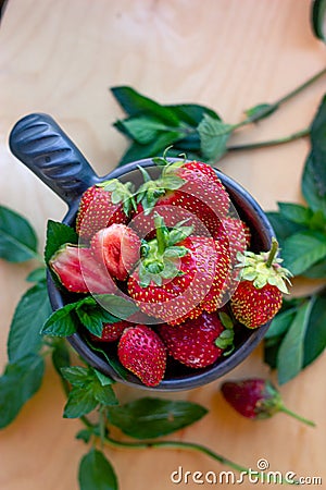 Ripe strawberries lie in a brown mug along with mint leaves on a wooden table among mint leaves Stock Photo