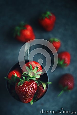 Ripe strawberries scattered around an iron mug. Dark photo Stock Photo