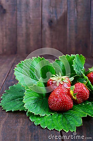 Ripe strawberry among the green leaves on a dark wooden table Stock Photo