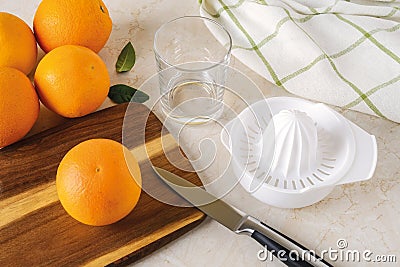 Ripe sweet oranges, plastic manual citrus juicer, fruit knife and empty glass on the kitchen table. Making freshly squeezed juice Stock Photo