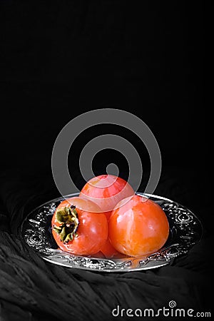 Ripe sweet persimmon fruit on silver tray, black background Stock Photo