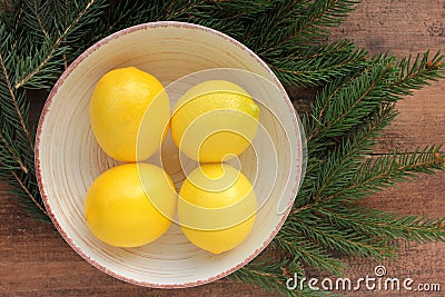 Ripe yellow lemons in a bowl on wooden table decorated with Christmas tree branches. Fresh citrus fruits on wood background. Stock Photo