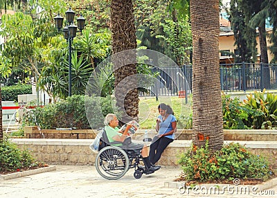 Asian nurse takes a man in a wheelchair for a walk in the park. Editorial Stock Photo