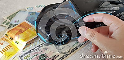 Young girl touches with her fingers a mirror of Black Bugatti Chiron metal toy standing with front wheels on paper money Editorial Stock Photo