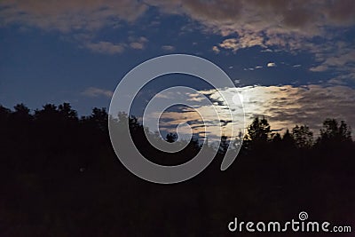 Rising moon behind cloud with colorful skyline Stock Photo