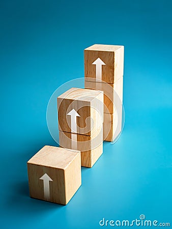 Rising up arrows shining on wooden cube blocks bar graph chart steps on blue vertical background, minimal style. Stock Photo