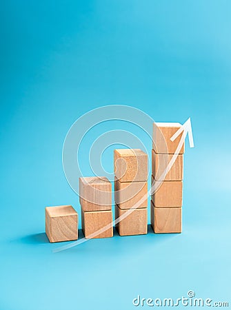 Rising up curved arrow draw on wooden cube blocks bar graph chart steps on blue background, minimal, vertical style. Stock Photo
