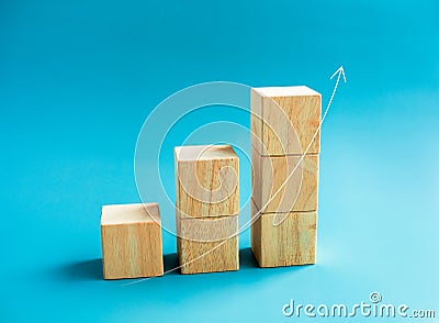 Rising up curved thin arrow draw on wooden cube blocks bar graph chart steps on blue background, minimal style. Stock Photo
