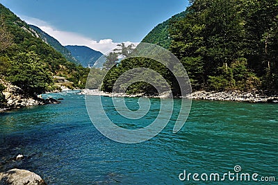 A river of aquamarine color flows between the slopes of the mountains covered with forest Stock Photo