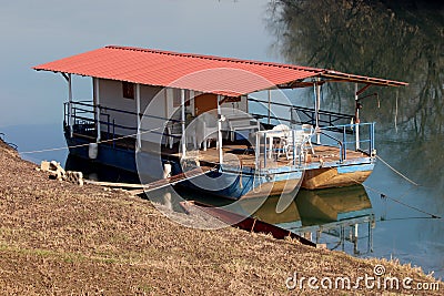 River barge converted into river boat house with improvised roof and terrace with white plastic chairs and tables Stock Photo