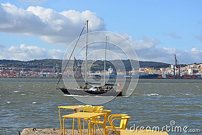 River boat on the Lisbon background. Yellow chairs and tables in riverside cafe in Almada. Portugal. Editorial Stock Photo