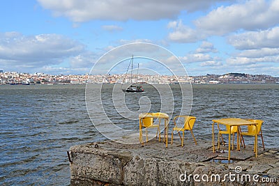 River boat on the Lisbon background. Yellow chairs and tables in riverside cafe in Almada. Portugal. Editorial Stock Photo