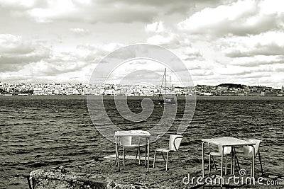 River boat on the Lisbon background. Yellow chairs and tables in riverside cafe in Almada. Portugal. Stock Photo