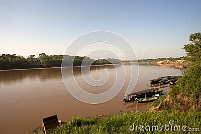 River Boats tied up to pier along river bank with view to other shore in Puerto Maldonado in Peru and the Amazon Stock Photo