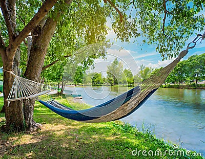 A riverside view with a hammock swaying gently in the breeze under shady trees Stock Photo