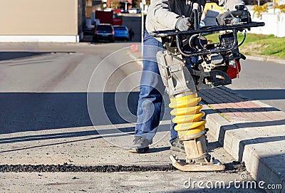 A road builder uses a vibration rammer to repair an asphalt road section Stock Photo