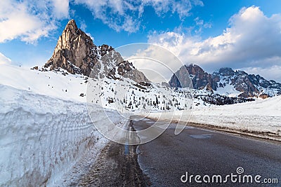 Road cleared of snow overlooked by a high rocky peak in the Alps in winter Stock Photo