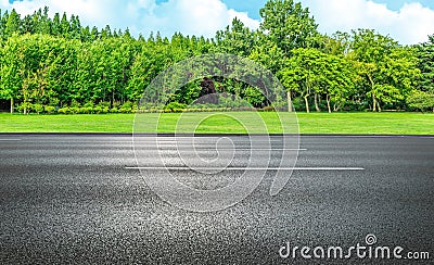 Asphalt straight street roadway of lanes with lines and green trees with blue sky in background. Stock Photo