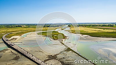 Road and colourful sand flats surrounding Le Mont Saint Michel during low tide, Normandy, Northern France Stock Photo