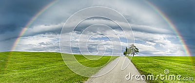 Road in a green hilly landscape with a rainbow Stock Photo