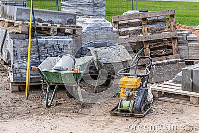 Road and pavement constuction work site with bricks piles, rammer machine and carts. Stock Photo