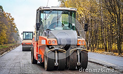 Road repair, compactor lays asphalt. Heavy special machines. Asphalt paver in operation. Side view. Closeup. Stock Photo