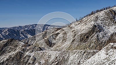 The road runs along a steep rocky snow-covered mountain slope Stock Photo