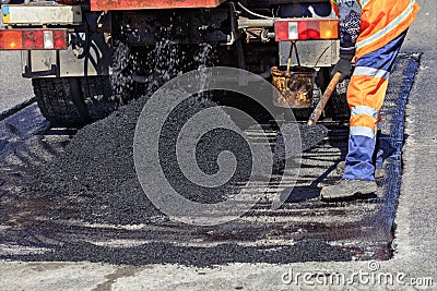 Road service worker rasbrasyvaet part of the asphalt with a shovel for patching the road Stock Photo