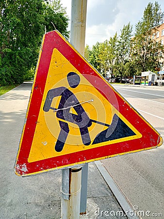 Road sign `Construction works`. The symbol is old, scuffed and dirty. Paint yellow and red. The black man is digging. Stock Photo