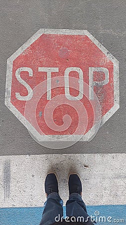 Road sign `Stop` painted on road with two standing feet in front Stock Photo