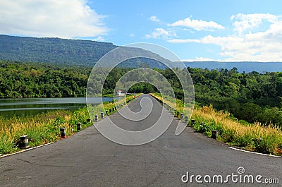 The road stretches along a beautiful river or lake, with mountains, blue sky, white cloud and green forests in the foreground Stock Photo