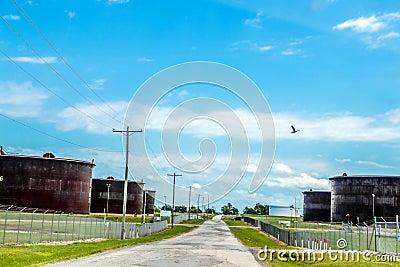 Road through tank farms with huge rusty petroleum tanks on either side and bird flying above in Cushing Oklahoma where most oil in Stock Photo