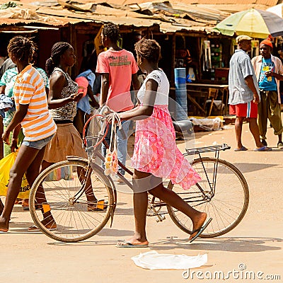 Unidentified local woman pulls a bicycle in a village in Guinea Editorial Stock Photo