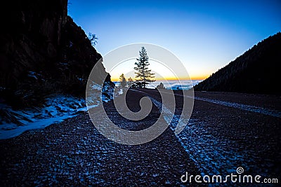 A road and a tree at sunrise atop a mountain Stock Photo