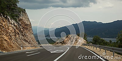 The road turns a mountain. Pointers on the pavement. Mountains, lake and clouds in the background Stock Photo