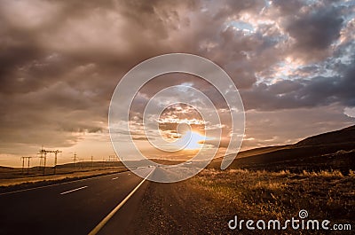 Road vanishing to the horizon under sun rays coming down trough the dramatic stormy clouds. Sunset at the mountain road. Azerbaija Stock Photo