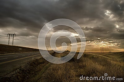 Road vanishing to the horizon under sun rays coming down trough the dramatic stormy clouds. Sunset at the mountain road. Azerbaija Stock Photo