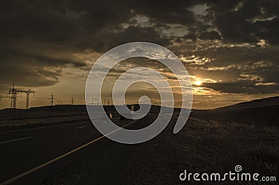 Road vanishing to the horizon under sun rays coming down trough the dramatic stormy clouds. Sunset at the mountain road. Azerbaija Stock Photo