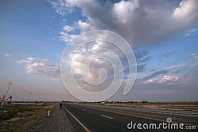 Road vanishing to the horizon under sun rays coming down trough the dramatic stormy clouds. Sunset at the mountain road. Azerbaija Stock Photo