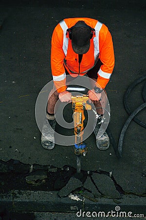 Road worker with a drill breaking up asphalt on the road Stock Photo