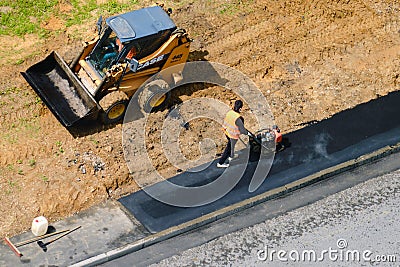 Road workers level the asphalt on the ground and lay it with a manual roller and excavator case - Moscow, Russia, may 21, 2020 Editorial Stock Photo