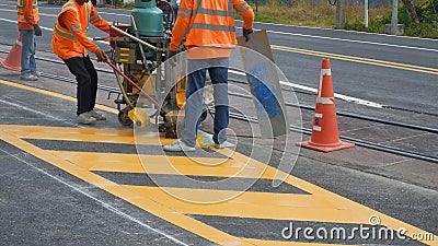Road workers with thermoplastic spray road marking machine are working to paint traffic yellow lines Stock Photo