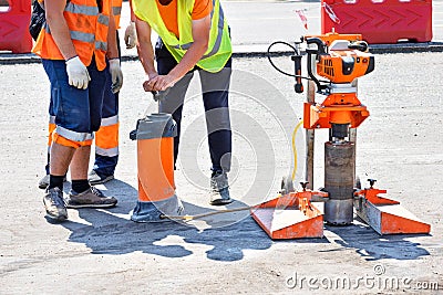 Road workers in reflective raincoats drill asphalt with a core drill Stock Photo
