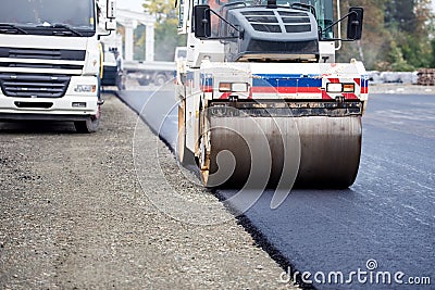 Road works, asphalting and laying fresh bitumen during construction works. Industrial heavy compactor Stock Photo