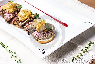 Roast beef with fried onions on pieces of baguette on white plate Stock Photo