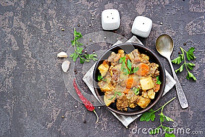 Roast, stewed beef with potatoes and carrots in a brown clay bowl on a dark concrete background Stock Photo